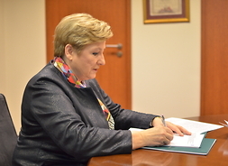 członek zarządu Elżbieta Lanc siedzi przy stole, podpisuje umowę na dofinansowanie projektyów w ramach RPO WM 2014-2020