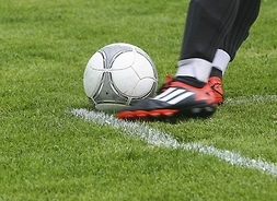 na zielonej murawie widać piłkę i nogi kopiącego gracza