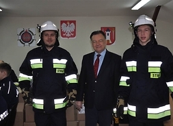marszałek obok niego stoją dwaj młodzi strażacy w nowym ubraniu