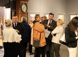 Grupa pracowników muzeum i gości rozmawiająca w sali z pocztówkami