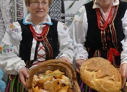 Dwie panie w tradycyjnych strojach prezentują chleby i wypieki