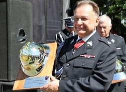 Marszałek trzyma w rękach tablicę z naklejonym srebrnym hełmem