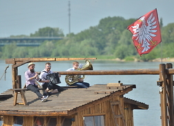 Trzech muzyków siedzi na drewnianym dachu statku