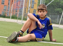 Chłopie w stroju sportowym siedzący na murawie boiska