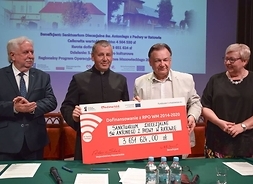 cztery osoby, w tym m.in. marszałek Adam Struzik, stoją, trzymają w ręku symboliczny czek na dofinansowanie kościoła w Ratowie