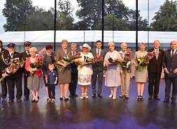 Osoby z wiązankami kwiatów stojące na scenie