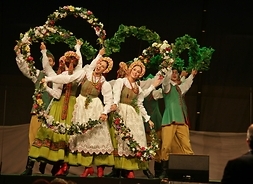 Członkowie zespołu Mazowsze na scenie - w rękach trzymają zielone wieńce