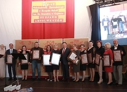 Zdjęcie przedstawia grubę osób pozujących do pamiątkowej fotografii z otrzymanymi dyplomami