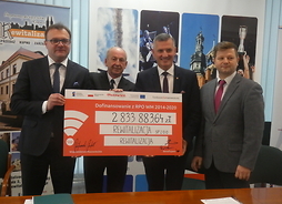 członek zarządu Rafał Rajkowski i beneficjenci trzymają w rękach symboliczny czek