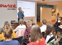 zastępca dyrektora Departamentu Kultury, Promocji i Turystyki Izabela Stelmańska, stojąc z mikrofonem w ręku opowiada młodzieży o Mazowszu