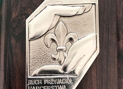 Srebrna honorowa odznaka przyjaciół harcerstwa - odznaka przedstawia dwie dłonie chroniące odznakę harcerską