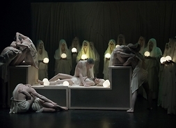 Aktorzy stoją z lampionami w dłoniach nad białą trumną