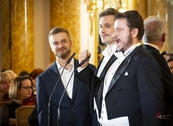 soliści Jakub Wocial, Daniel Mirosław, Sławomir Naborczyk stoją na scenie przy mikrofonach