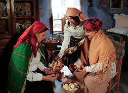 Trzy kobiety w tradycyjnych strojach ludowych zajmują się zdobieniem jaj wielkanocnych.