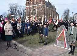 Członek zarządu Elżbieta Lanc przemawia w obecności wielu mieszkańców, podczas uroczystości przy tablicy na Placu Kościelnym.