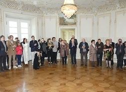 Uczestnicy spotkania z twórcami filmu pt. „Pani na Korczewie” stoją w sali pałacowej - pokazani w dużym planie.