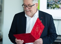 Burmistrz Grodziska Mazowieckiego Grzegorz Benedykciński stoi i czyta z folderu