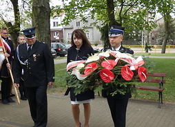 Członek zarządu Janina Ewa Orzełowska składa biało-czerwony wieniec. Towarzyszą jej dwaj strażacy
