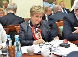 Przy stole klubu radnych PO siedzi członek zarządu Elżbieta Lanc, która przegląda  dokumenty. W tle inni radni
