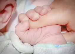 Rączka niemolęcia, która ściska palec dorosłego. Widać jasne ubranko dziecka.