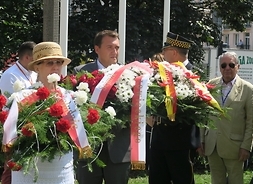 Z wieńcami w dłoniach stoją trzy osoby, w tym wiceprzewodniczący sejmiku Marcin Podsędek