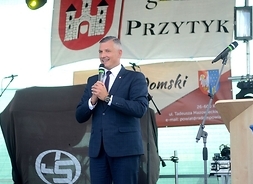 Wicemarszałek Rafał Rajkowski stoi na scenie z mikrofonem ręku przy ustach. Za nim w tle widac mównicę i baner z herbem Przytyku