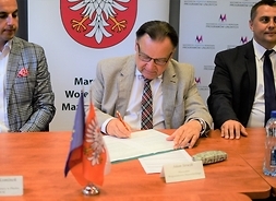 Za stołem siedzi trzech uczestników aktu podpisania umów. W środku kadru umowę podpisuje marszałek Ada Struzik.
