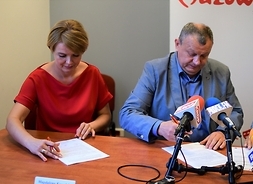 Siedząc za stołem, umowę podpisują przedstawiciele władz gminy Zawidz, wójt i skarbnik.