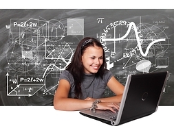 studentka siedzi przy laptopie, w tle tablica ze wzorami matematycznymi