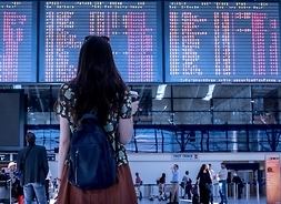 kobieta z plecakiem stoi przed tablicą odlotów na lotnisku