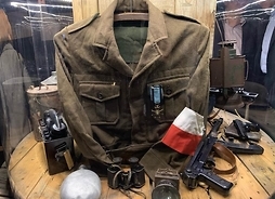 Ekspozycja wystawy, na którą składa się mundur wojskowy, lornetka, menażka, telefon stacjonarny