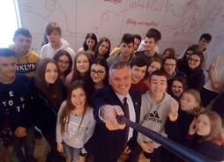Zdjęcie z góry na marszałka Rajkowskiego. Za nim widać grupę uczniów. Marszałek trzyma kij do selfi i uśmiecha się, patrząc w aparat
