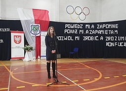 Członek zarządu Janina Ewa Orzełowska stoi przed mikrofonem. Za nią w tle są banery z godłem województwa oraz flagą Polski