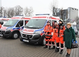 Pamiatkowe foto w pełnym planie na placu przed jednostką, obod dwóch nowych ambulansów stoją w rzedzie trzej ratownicy i Elżbieta Lanc.