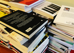 Na stole leżą ułożone w kilku stosach książki nominowane do Nagrody Literackiej im. Witolda Gombrowicza 2020 - inne ujęcie.