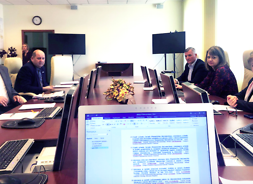 Przy owalnym stole prezydialnym siedzą członkowie zarządu. Na pierwszym planie widać monitor komputera z wyświetlonym dokumentem
