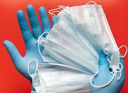 Kilka maseczek ochronnych białych trzymana przez dwie dłonie w niebieskich rękawiczkach ochronnych.