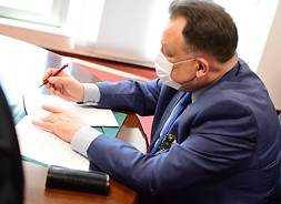 Widoczny z boku Marszałek Adam Struzik siedzi za stołem i podpisuje prawą reką list intencyjny.