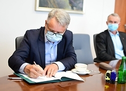 Prezes Mirosław Maliszewski siedzi za stołem i prawą ręką podpisuje list intencyjny. Patrzy na to siedzący po prawej skarbnik Witold Piekarniak.