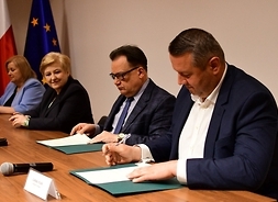 Prezydent Ostrołęki Łukasz Kulik siedzi za stołem i podpisujelist intencyjny, za nim po jego prawej siedzą  marszałek Adam Struzik  i Elżbieta Lanc.