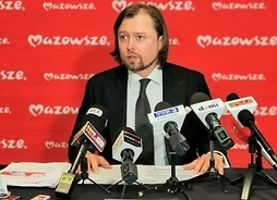 Występuje dyrektor MJWPU Mariusz Frankowski, siedząc za stołem przed mikrofonami.