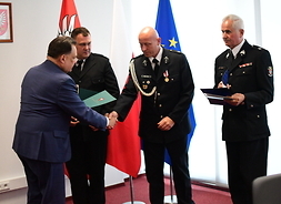 Marszałek gratuluje druhom, w tle flagi Mazowsza i UE
