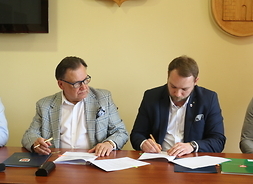 Marszałek i zastępca burmistrza siedzą obok siebie przy stole i podpisują dokumenty
