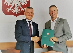 wicemarszałek Rafał Rajkowski i wójt gminy Klwów Piotr Papis stoją obok siebie trzymając teczkę z dokumentami urzędowymi.