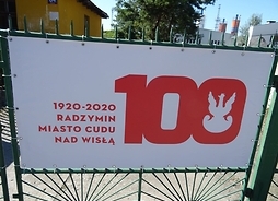 Tablica informująca o uroczystościach, z czerwonym napisem na białym tle: 100 <-> 1920-2020 Radzymin - Miasto Cudu nad Wisłą
