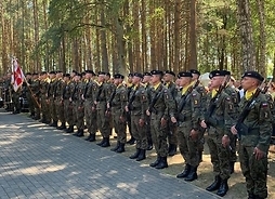 Kilkudziesięciu żołnierzy w polowych mundurach, stoi w rzędzie podczas uroczystości .