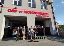 Strażacy ochotnicy stoją przed murowanym budynkiem - siedzibą OSP w Mokobodach