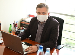 Przy stole na fotelu przed laptopem siedzi w maseczce ochronnej przewodniczący klubu radnych Koalicja Obywatelska Krzysztof Strzałkowski.