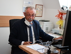 Radny Krzysztof Skolimowski siedzi na fotelu przy stole przed ekranem komputera.