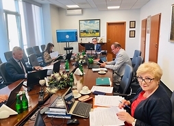 Pięć osób siedzi po obu stronach długiego stołu w sali konferencyjnej, przed nimi laptopy i rozłozone dokumenty.